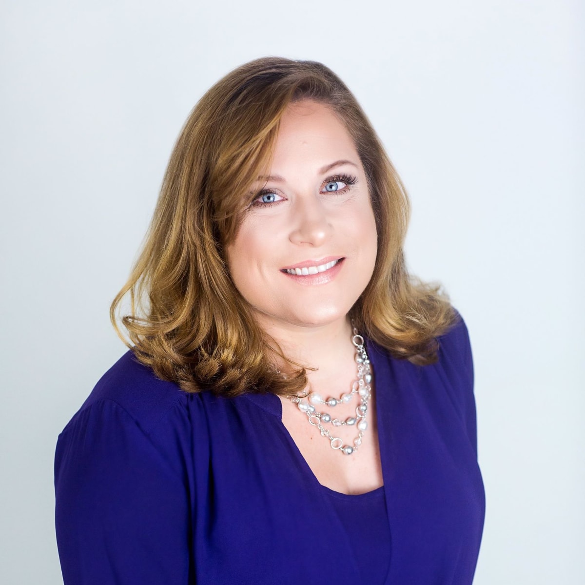 smiling light skinned woman with bright eyes and caramel colored hair wearing a blue blouse