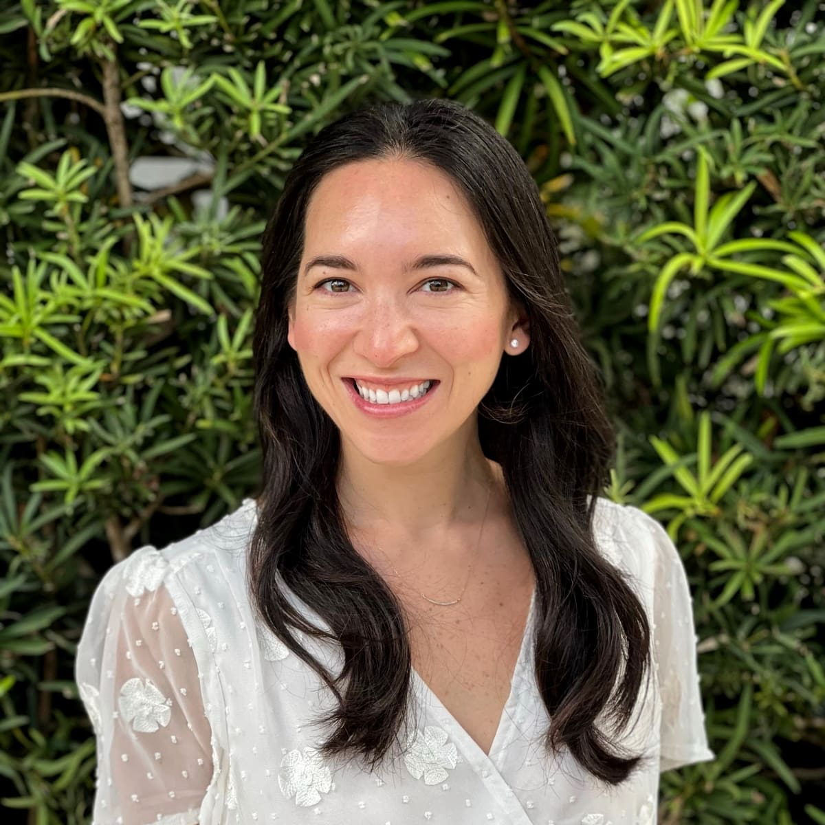 headshot of Emi Ortiz, a beautiful smiling light skinned woman with long, dark hair and a white blouse